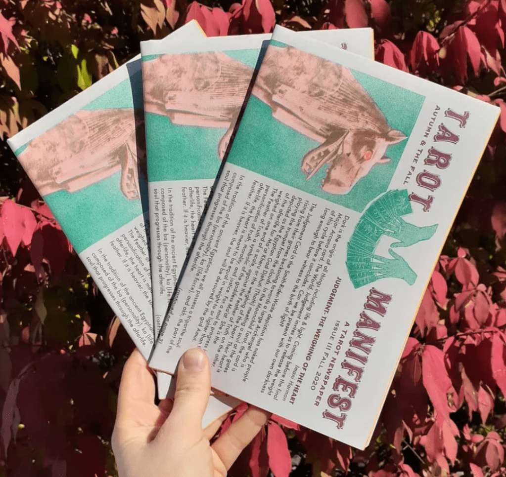 A hand holding copies of the Tarot Manifest zine.